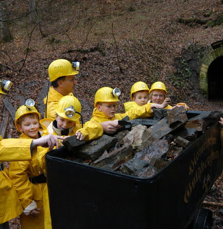 Besuchergruppe neben einem Wagon, der mit Steinen befüllt ist direkt vor dem Eingang in den Stollen.