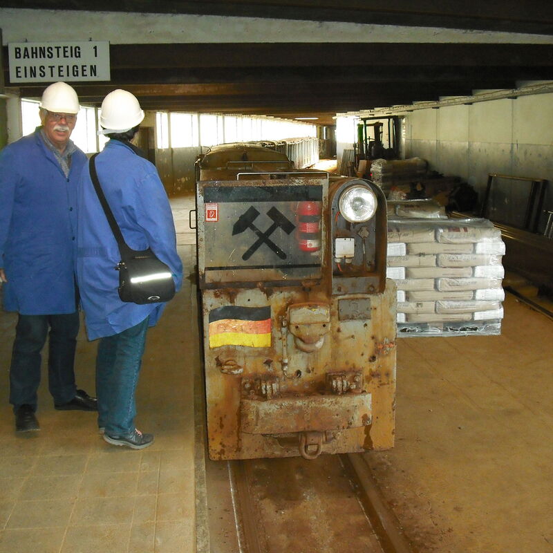 Das Bild zeigt zwei Menschen in Schutzkleidung neben einer Grubenbahn.