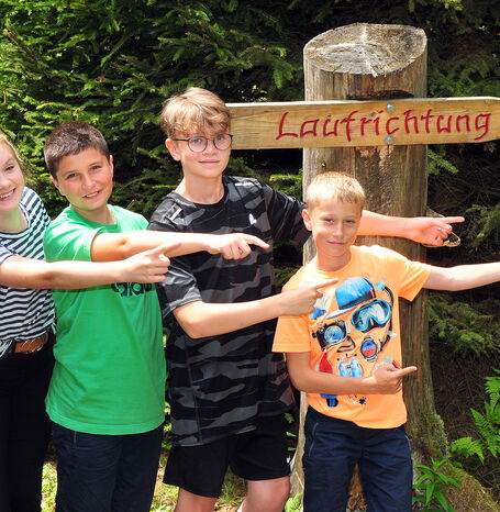 Vier Kinder, die vor einem Schild stehen, das die Laufrichtung anzeigt.