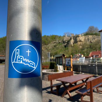Das Wegsymbol für den Klosterpfad ist blau mit einem Kreuz und einem Umriss der Burg drauf.